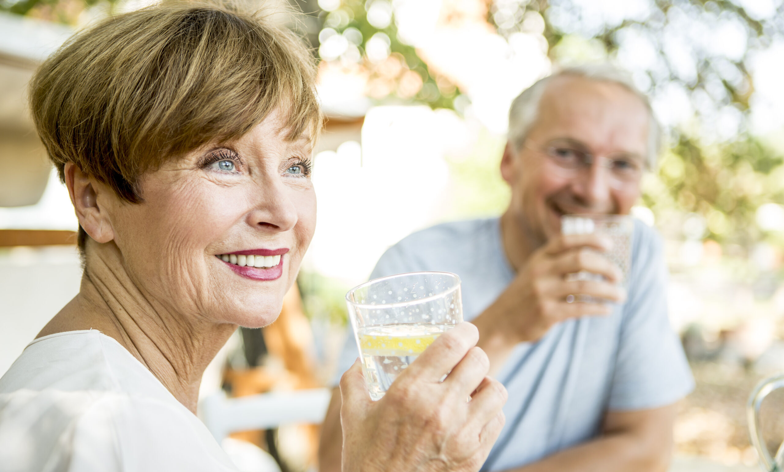 Femme âgée souriante buvant un verre d'eau de source naturelle abenakis avec son mari en arrière-plan